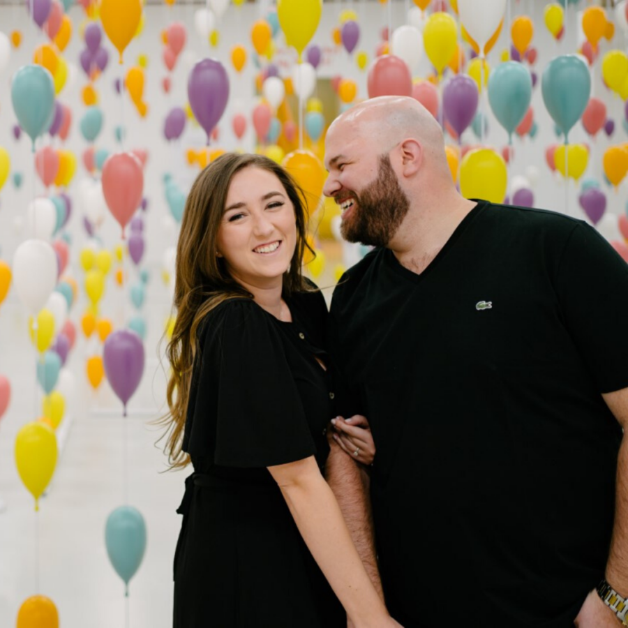 couple dressed in black posing in front of green, yellow, pink, and purple balloons