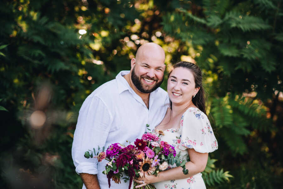 Couple in white clothes posing against vivid green trees