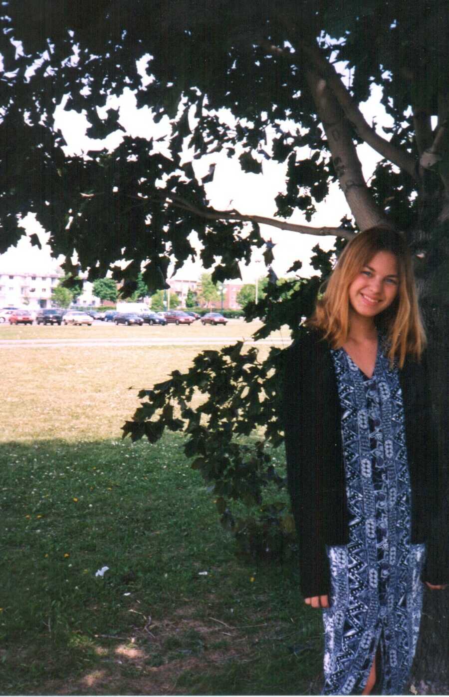 teenage girl in a blue dress posing in front of a tree