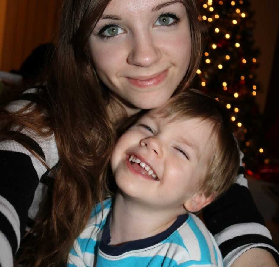 Young mom takes a selfie with her oldest son during Christmastime with a Christmas tree behind them