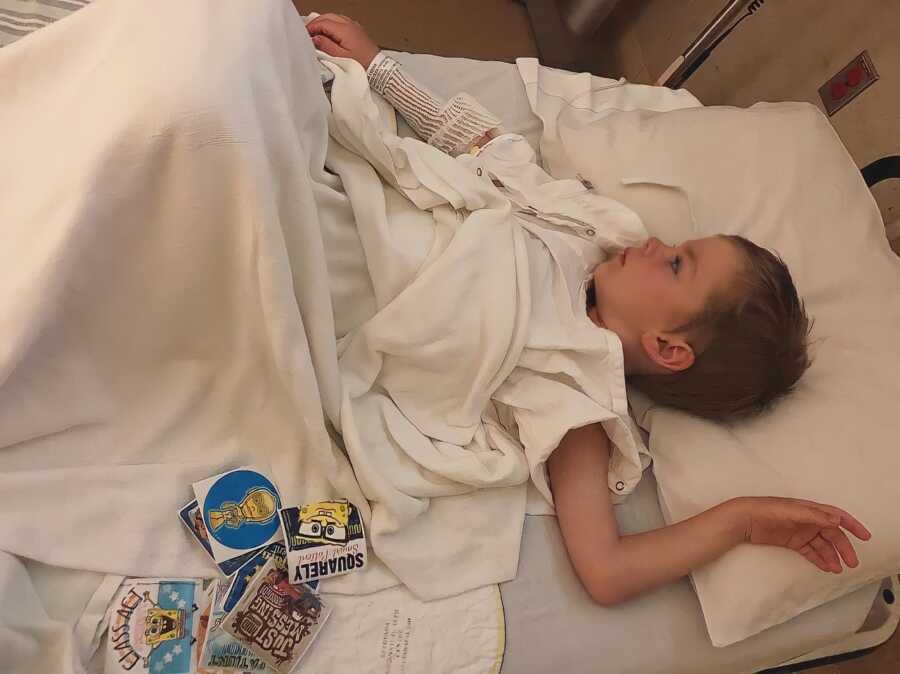 Little boy with an infection lays down in a hospital bed with a bunch of stickers next to him