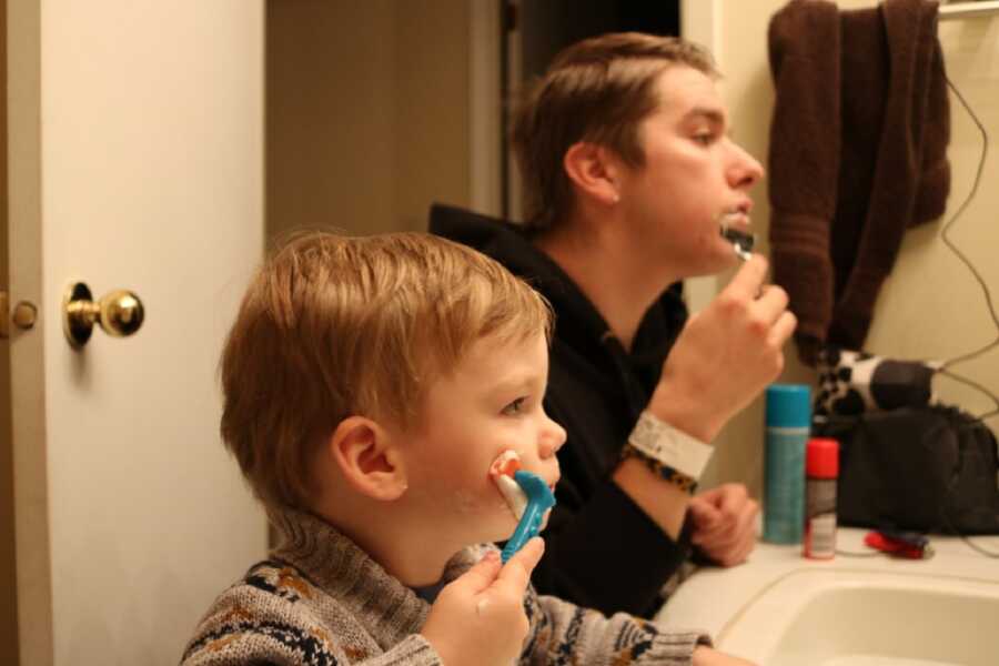 Young son copies his father shaving in the mirror with a fake razor
