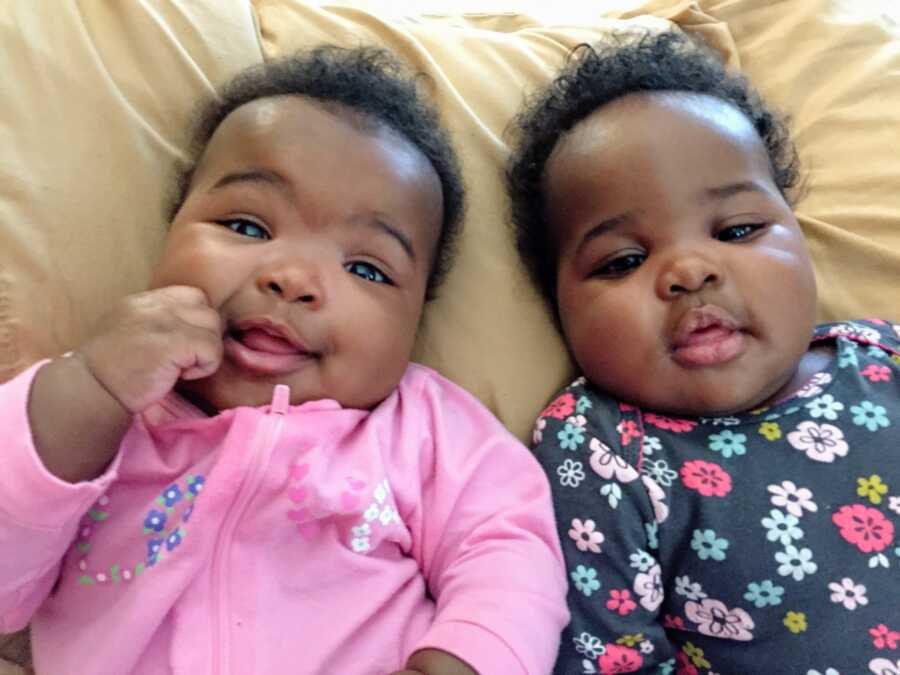 Twin girls stare into the camera while laying next to each other in bed