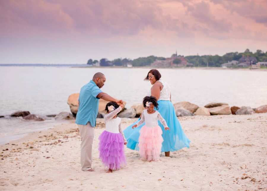 Family of four dance around on the beach with a pink sunset behind them