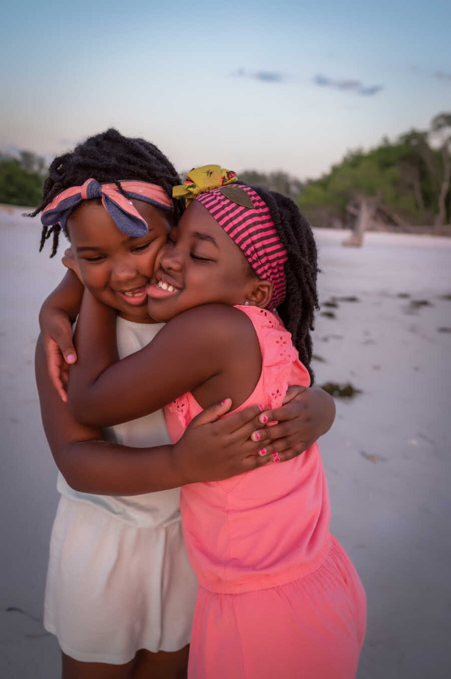 Twin daughters with autism embrace each other on the beach during family photos