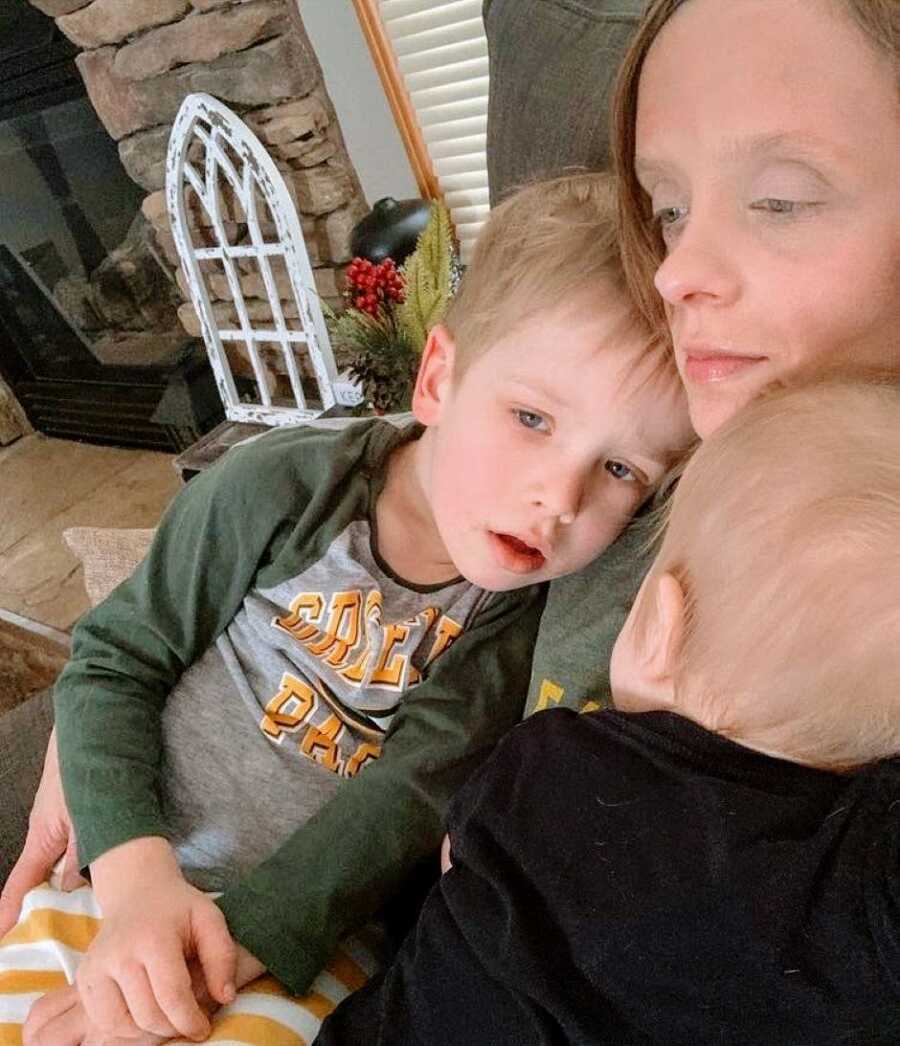 Mom lays down on the couch with her two sons, looking worn out and exhausted