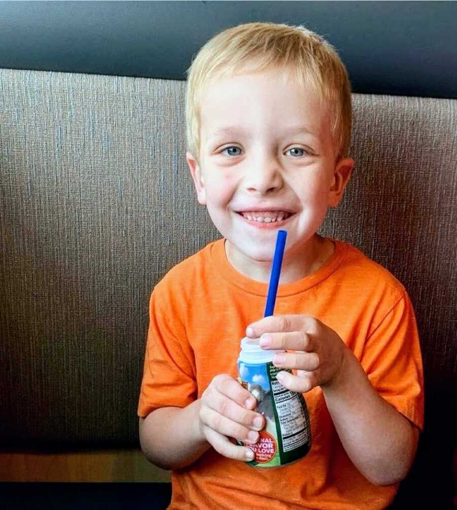 Little boy with autism in a bright orange shirt smiles big while drinking milk from a straw at a restaurant