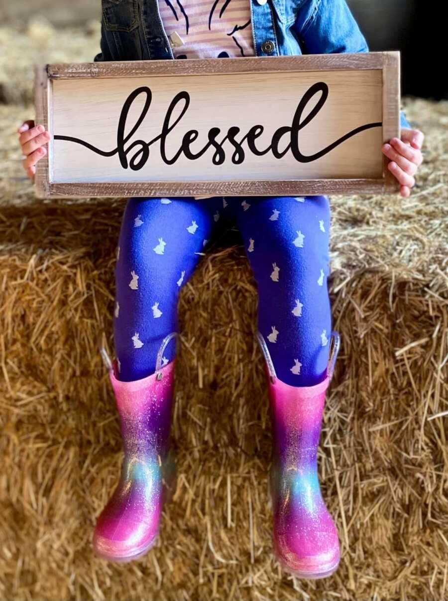 little girl sitting on a stack of hay holding a sign that says blessed