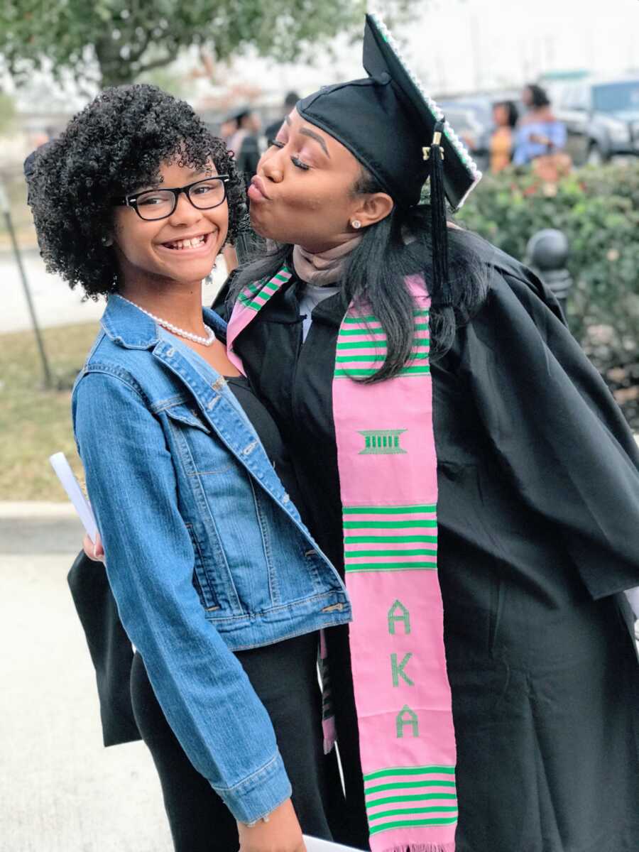 mother graduates from college and kisses daughter's cheeks while wearing graduation gown and cap