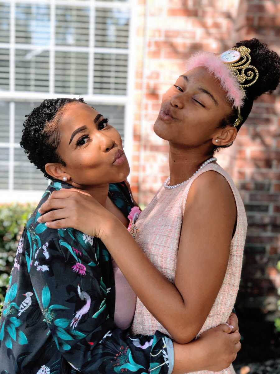 Mom and daughter do kissy faces at the camera while the daughter wears a crown on her birthday