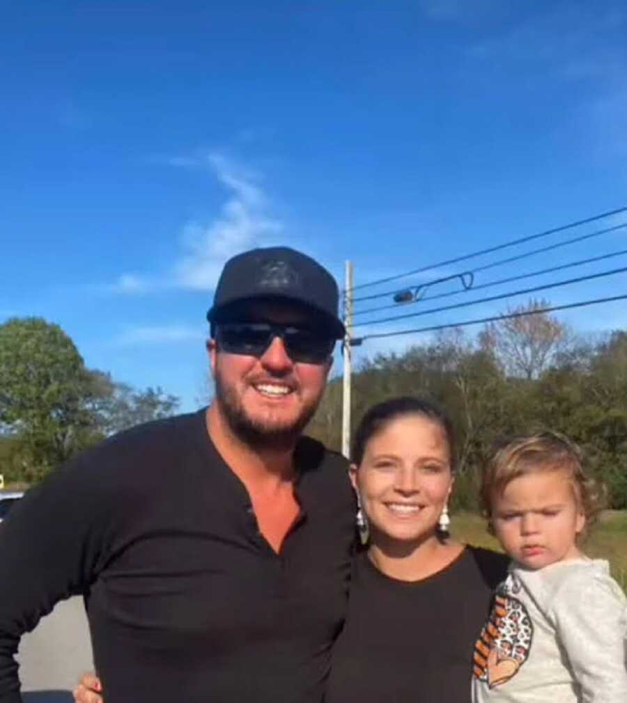 Luke Bryan posing next to a single mother and her son after helping them change a tire 