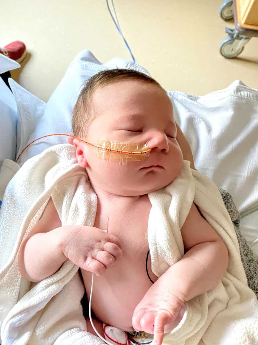 在医院里，一个带着喂食管的新生男婴安静地睡在母亲的怀里