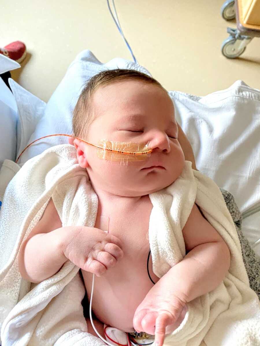 Newborn baby boy with a feeding tube sleeps peacefully in his mother's arms in the hospital