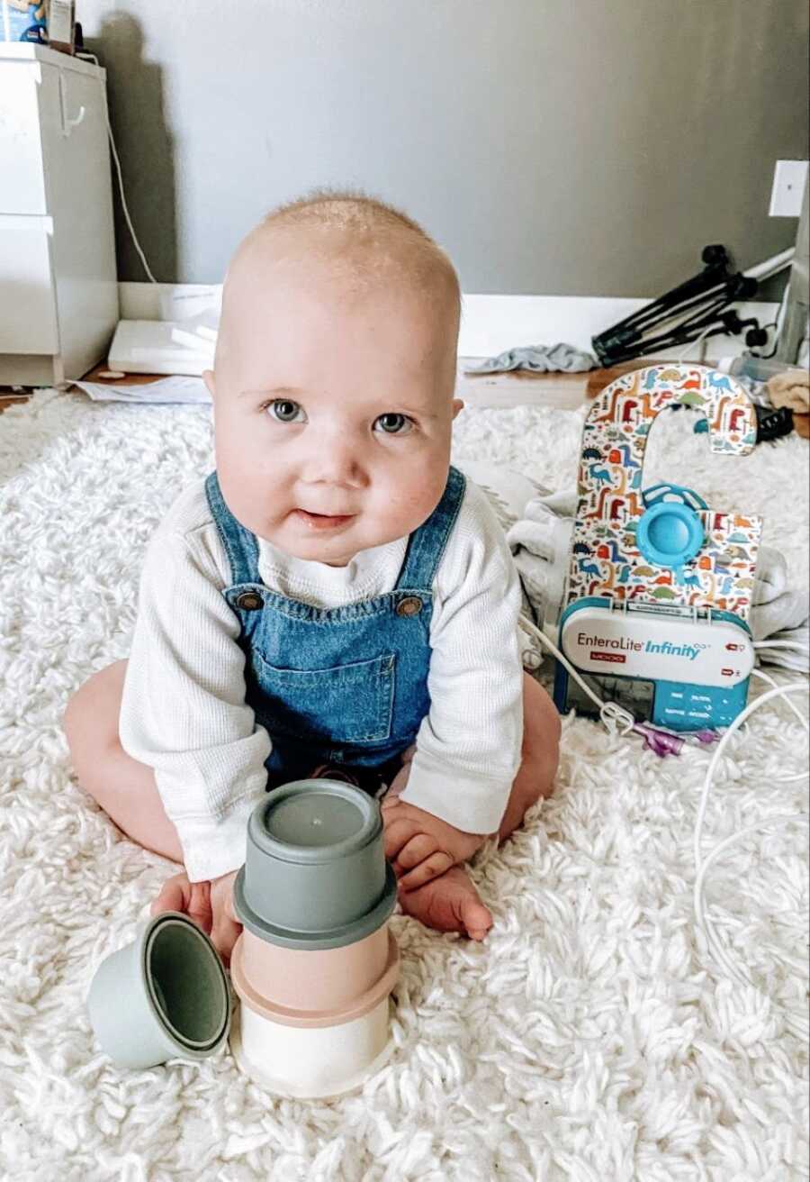 Little boy with rare chromosomal deletion looks at his mom while playing on the floor in denim overalls