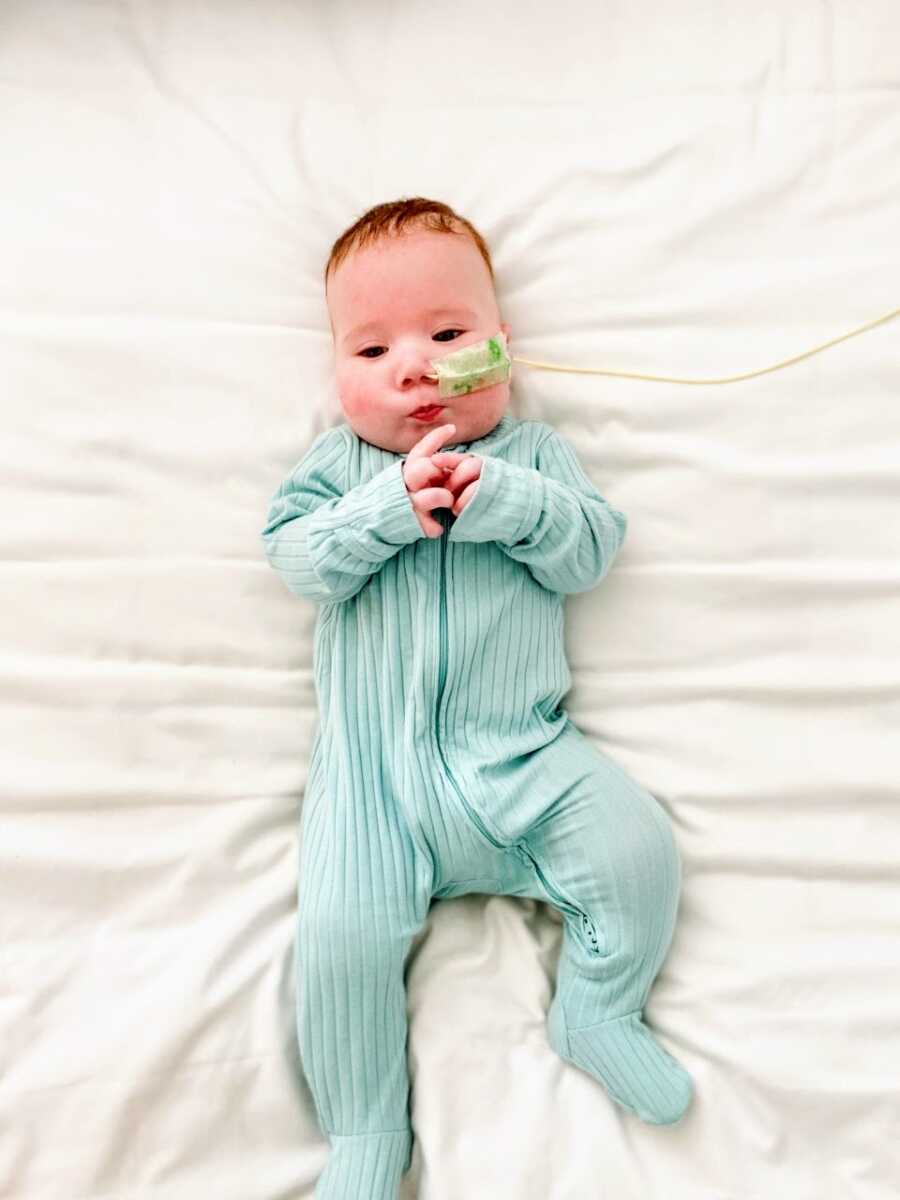 Little boy with rare chromosomal deletion lays on his back on a white blanket with a feeding tube in