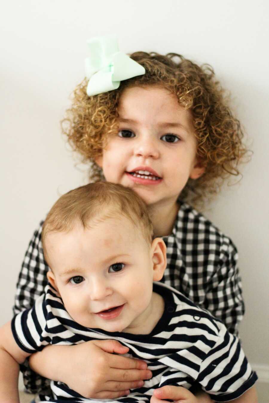 brother and sister posing together against a white wall