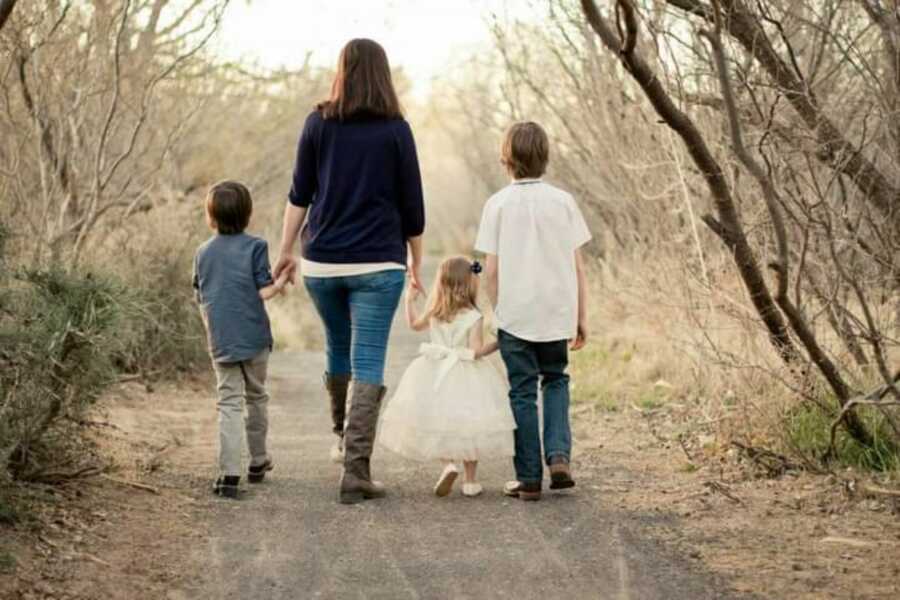 Prison wife takes a family photo with her three kids while walking down a road together, their backs turned to the camera