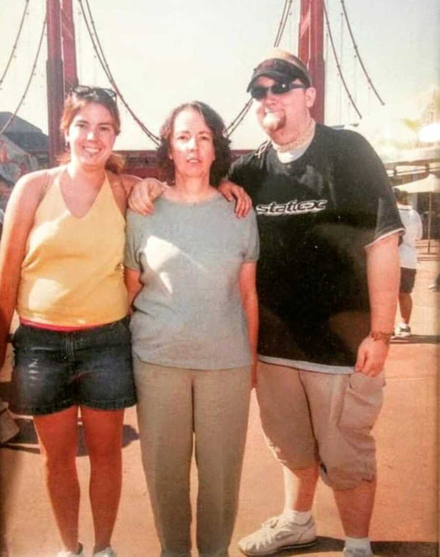 Woman takes a photo with her mom and brother while wearing a yellow tank top and denim shorts