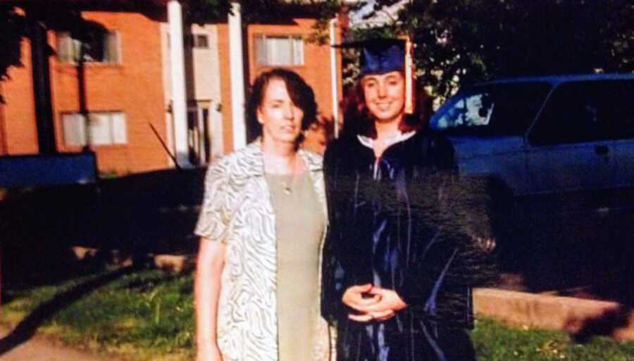 Young girl takes a photo in her cap and gown with her mom before her high school graduation ceremony