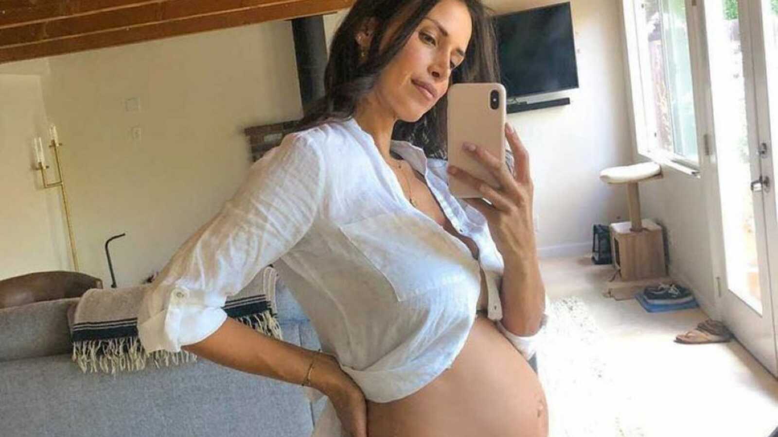 怀孕失败后，一名妇女在镜子前炫耀她裸露的怀孕肚