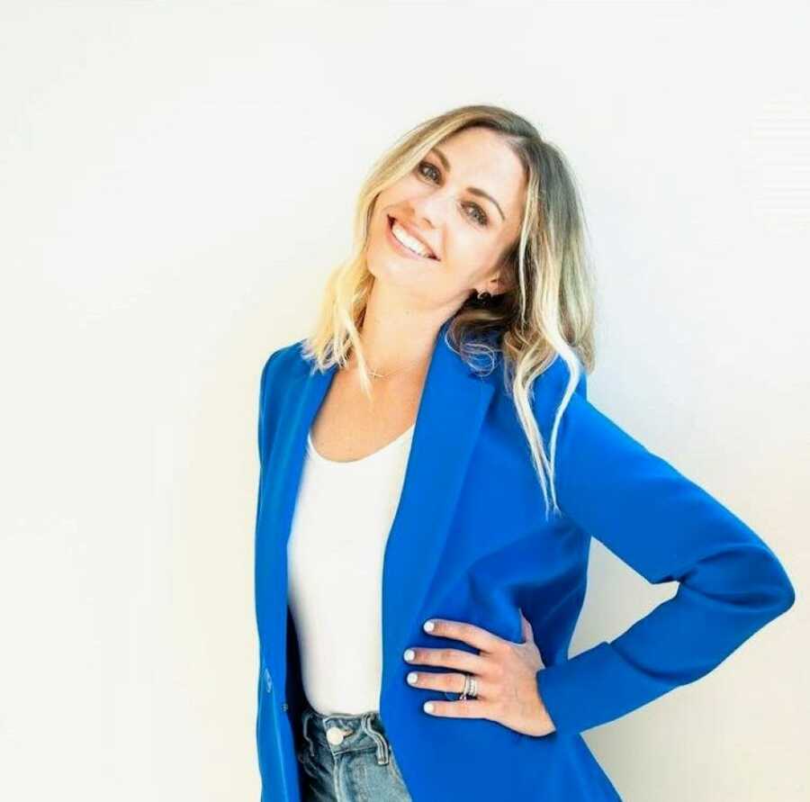 Woman smiling with one hand on her hip wearing a blue blazer jacket and white top. 