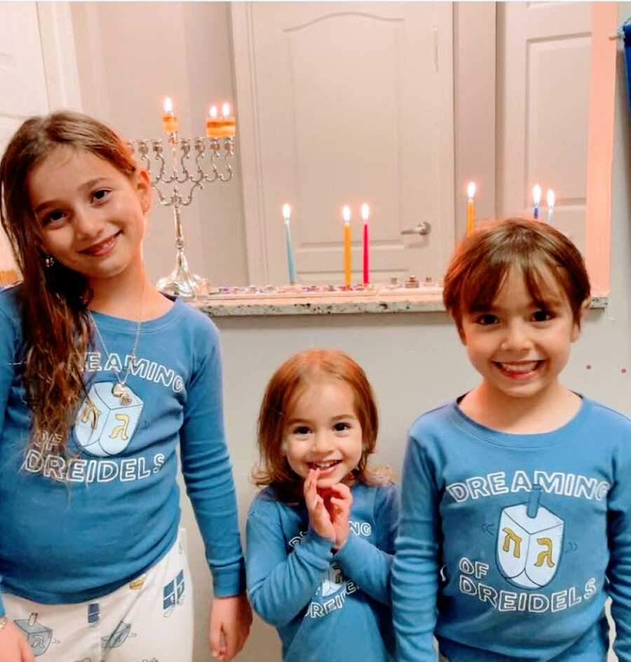 Mom takes photos of her daughter in matching Hanukkah pajamas with a lit menorah behind them