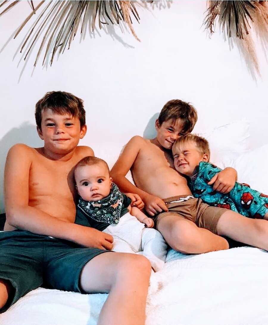Boy mom snaps a photo of her four sons cuddling in bed together after a long day of play