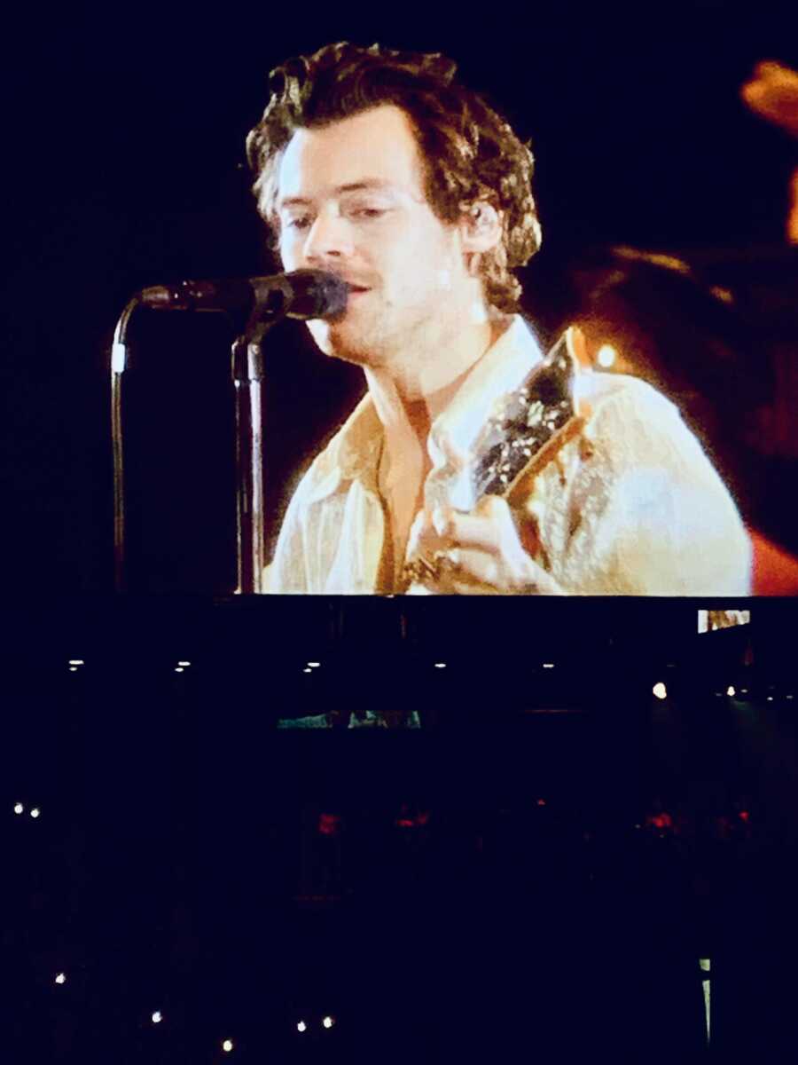 harry styles singing and playing his guitar at his concert