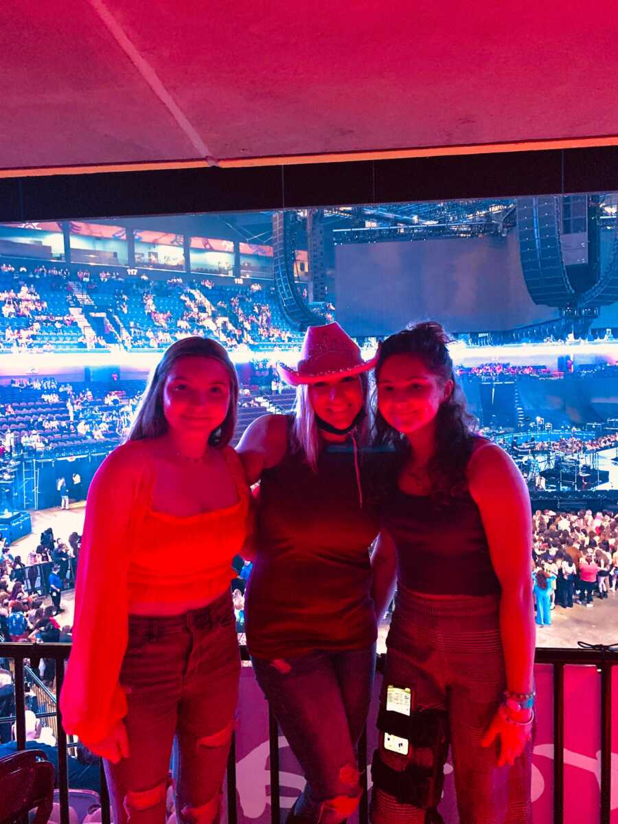 Mom, daughter, and daughter's friend smiling and happy at Harry Styles concert