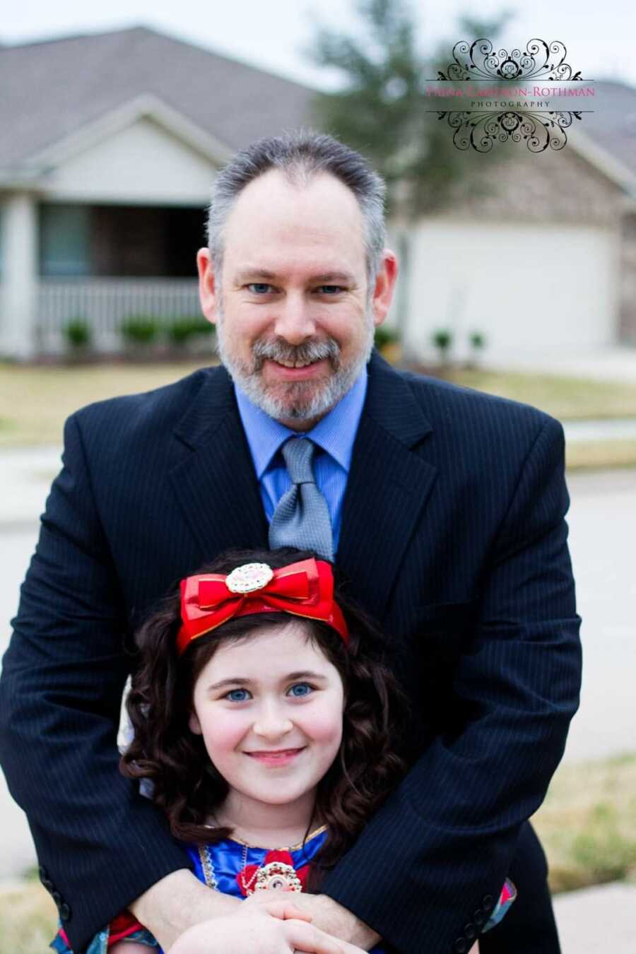 Dad stands in a suit with his special needs daughter dressed as Snow White before a Daddy Daughter Dance