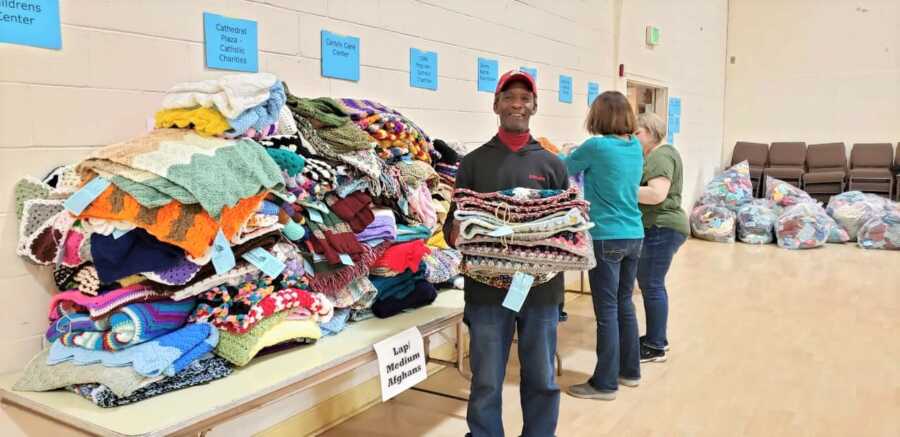 Larry stands next to a table full of his crochet creations for the homeless.