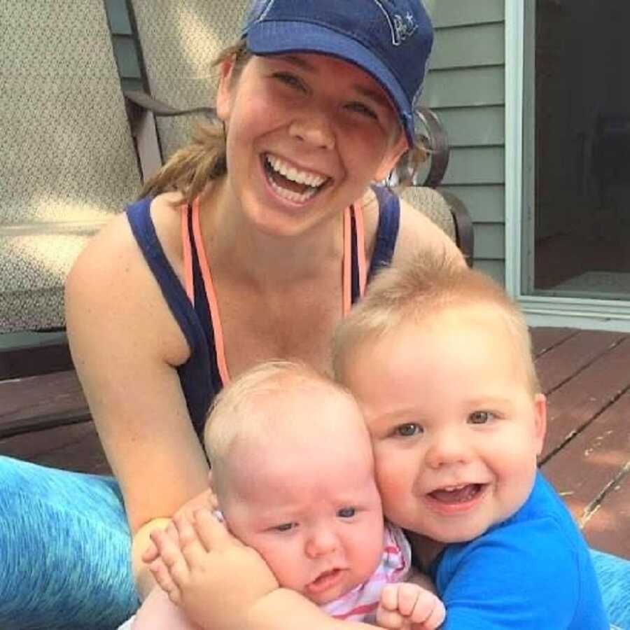 Mom takes a picture with her two young babies hugging.