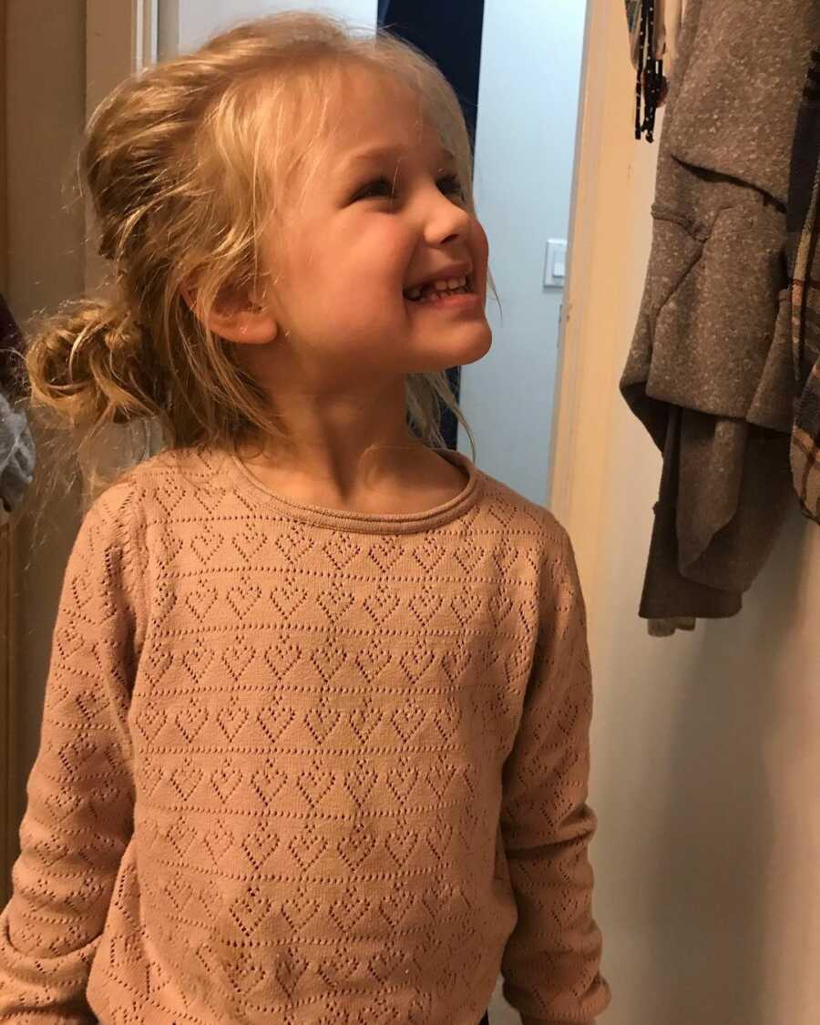Evie wears a pink heart sweater and a big smile. 