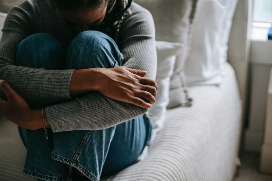 woman embracing knees on bed