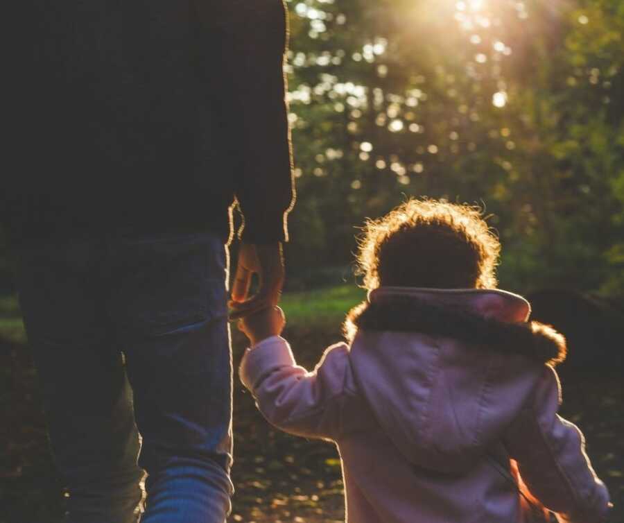 Toddler girl walks hand in hand with father. 