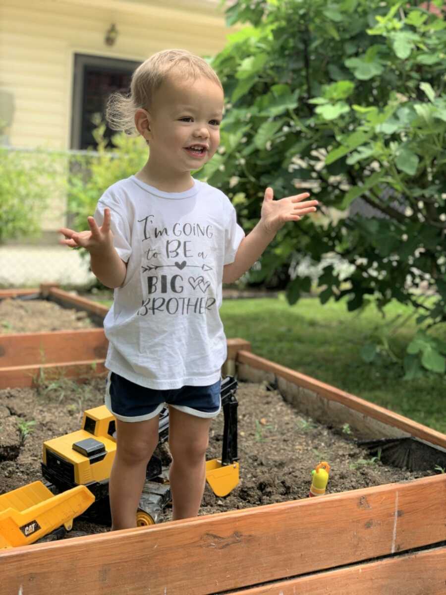 Big brother proudly displaying his big brother announcement shirt amid his beloved construction vehicle collection.