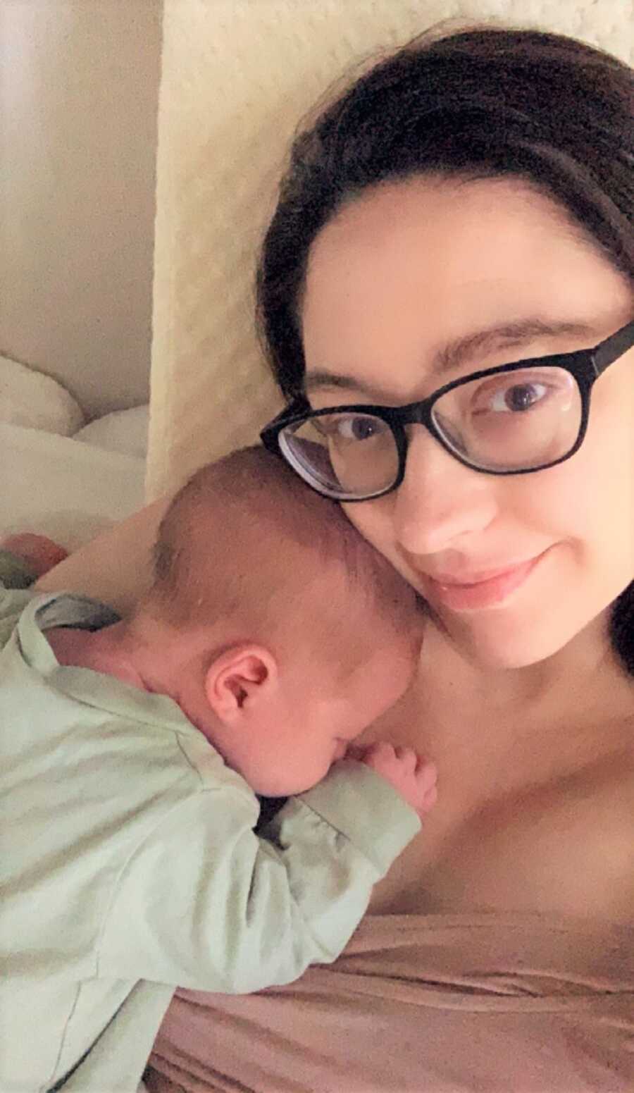 Baby sleeps on Mom's chest while she smiles at the camera. 