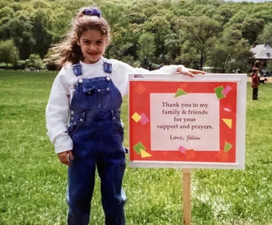 child wearing overalls standing next to a sign