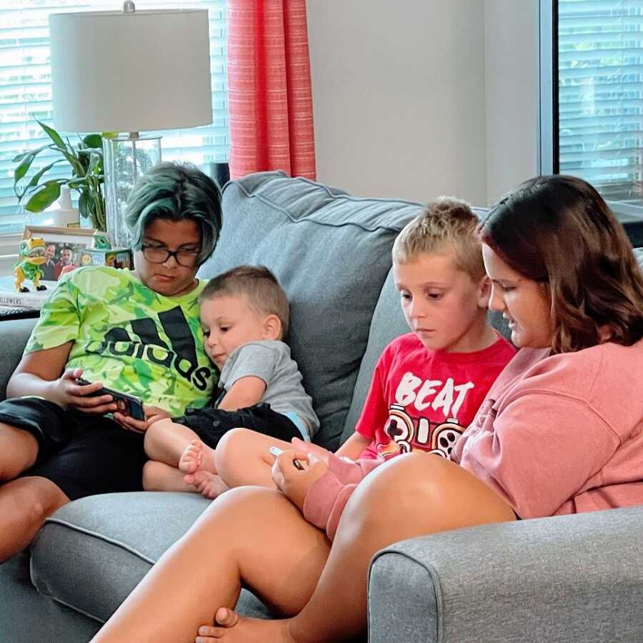 Four siblings sit together on a couch playing on phones