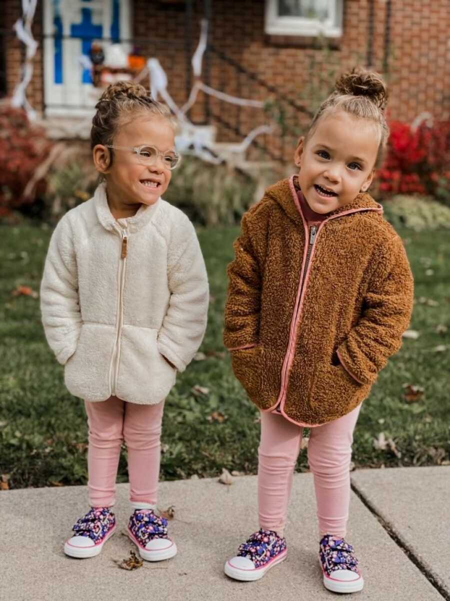 这对双胞胎女孩穿着粉色的打底裤和温暖的夏尔巴人夹克，开心地站在外面