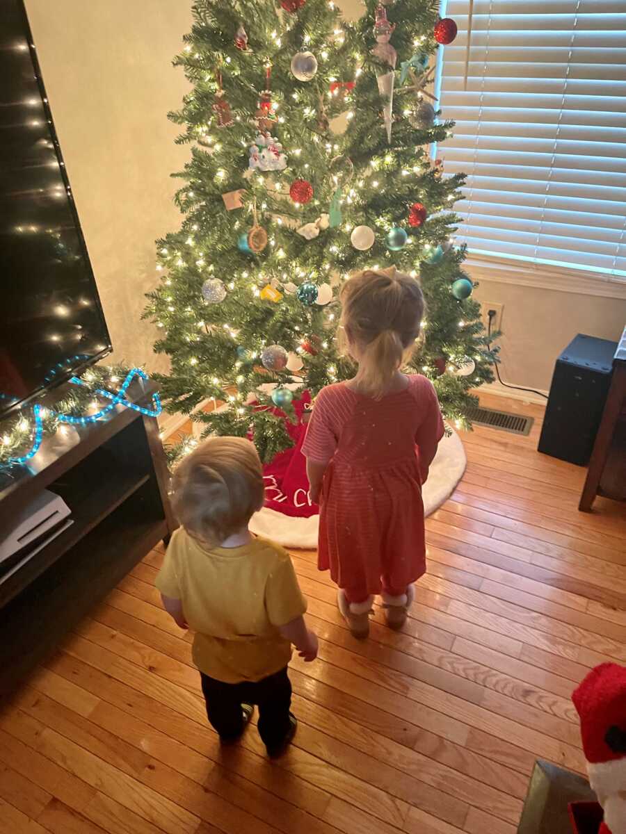 a little boy and girl stand in front of a christmas tree after losing their mom the year before 