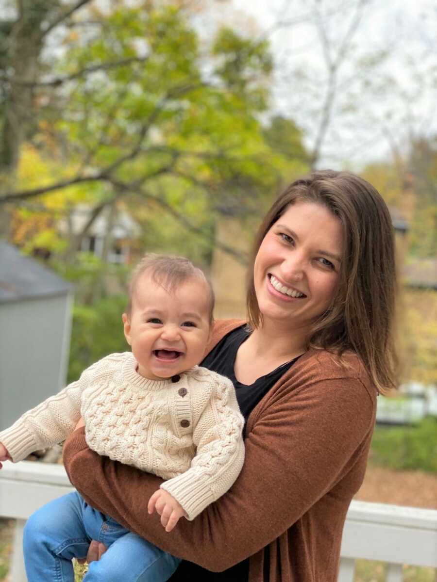 Michelle holds a laughing Sami and smiles at the camera. 