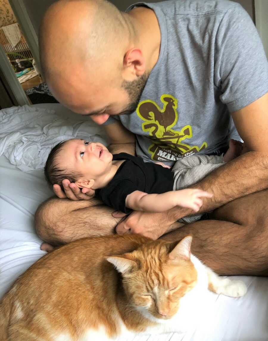 Sami's dad holds him in his lap, with one the family cats snuggled close by.