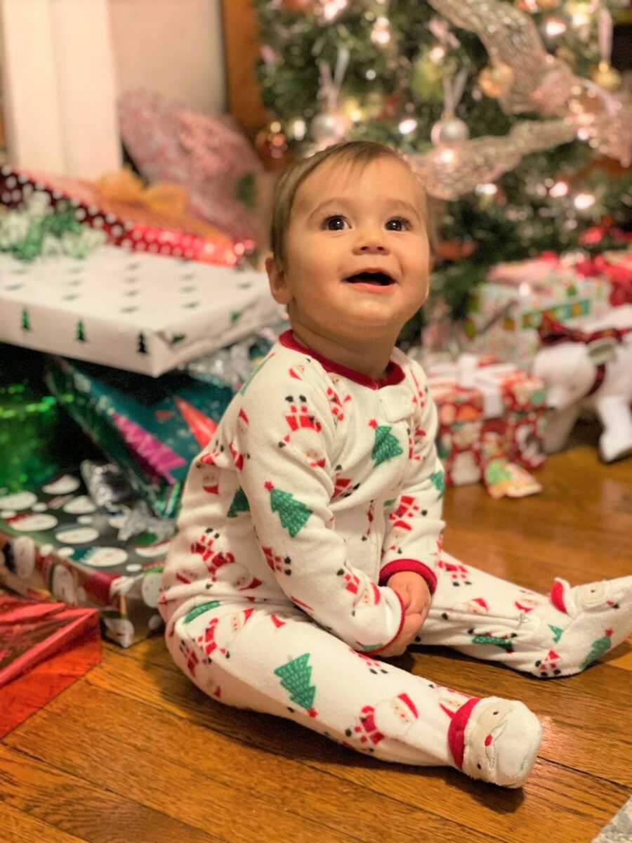 萨米坐在圣诞树前拿着礼物，穿着可爱的圣诞连体衣。