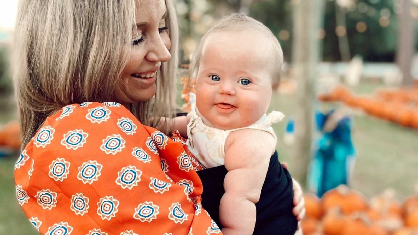 mama in a red dress holding her baby girl while standing in a pumpkin patch