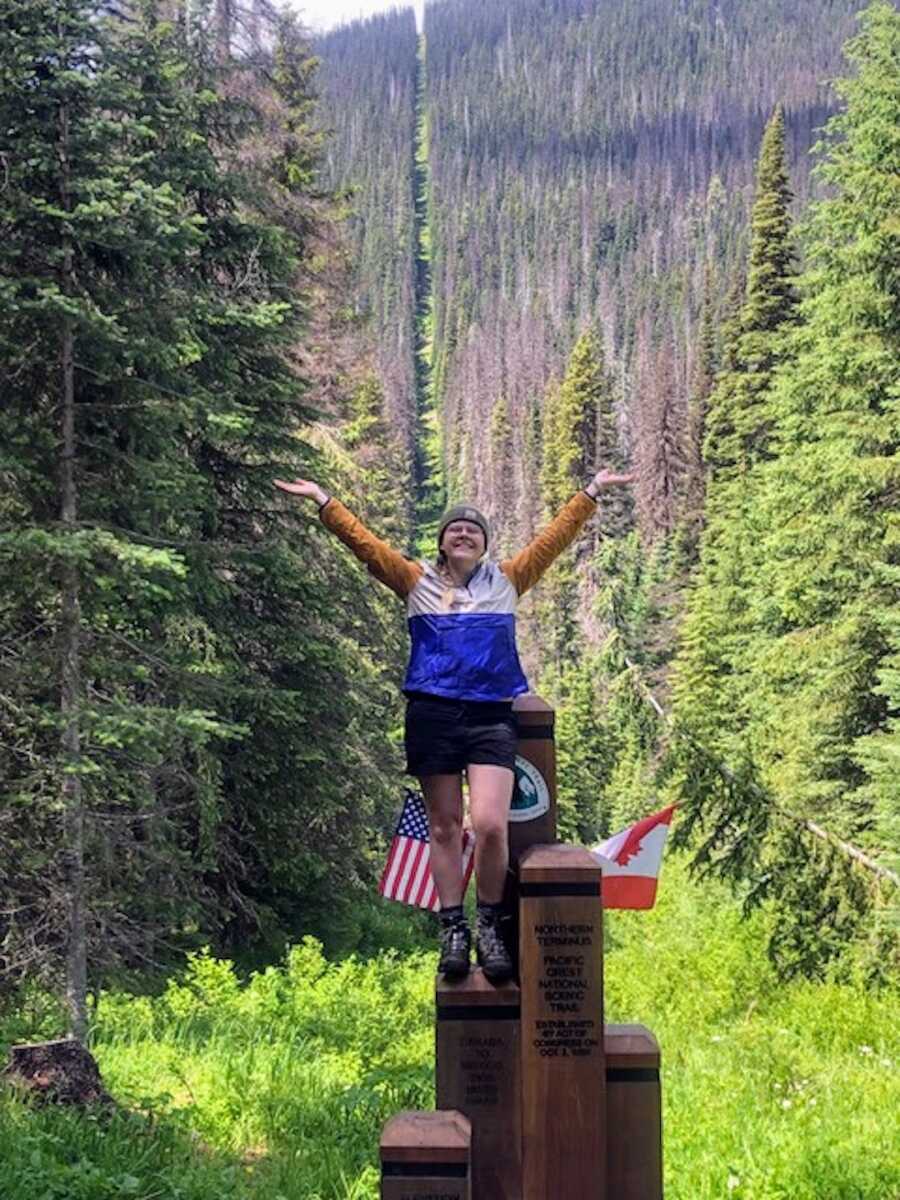 Woman stands on a wooden structure out in the forest