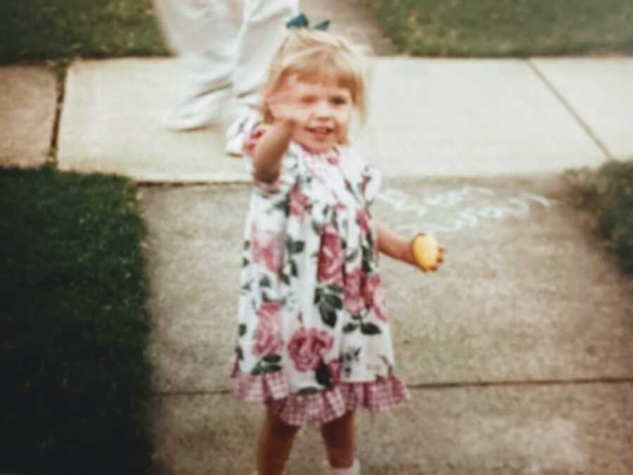 Toddler wearing a pink floral dress waves at camera