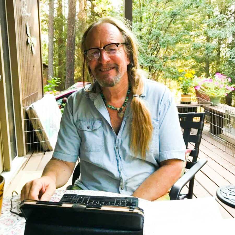 woodcarver sitting outside on his deck wearing a blue button down