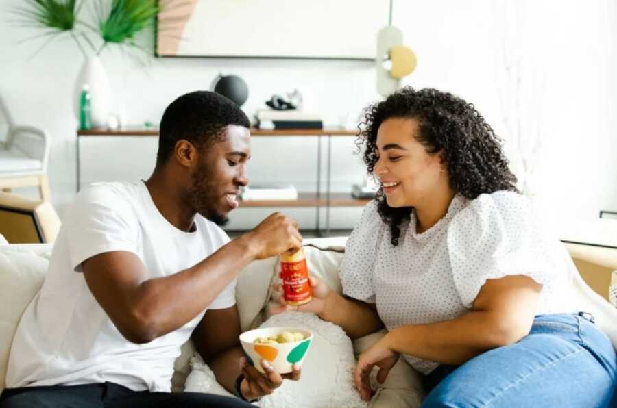 couple sitting on the couch sharing their food happily