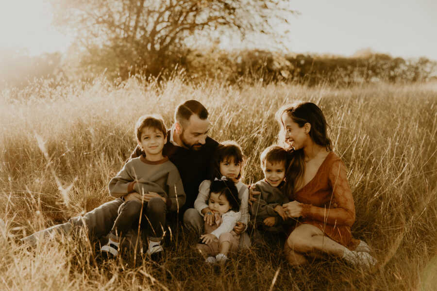 Pero family pictures sitting in the grass smiling at each other. 